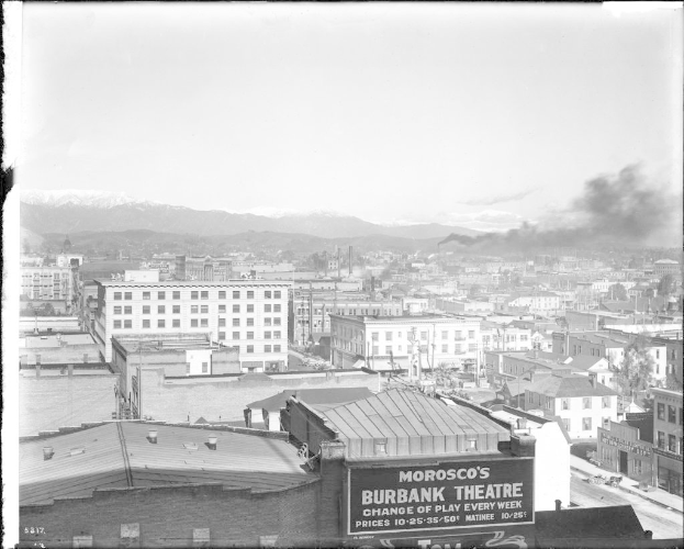 Ein Schwarz-Weiß-Bild einer Fabrik mit Rauch, der aus ihrem Schornstein kommt, umgeben von Gebäuden.