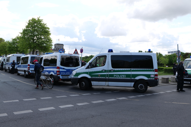 Eine Gruppe von Polizeiwagen, die entlang einer Straße geparkt sind, mit einem Radfahrer im Vordergrund und Gebäuden, Bäumen, Schildern im Hintergrund.
