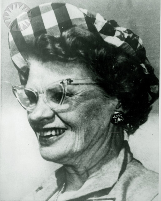 Eine lachende Frau mit Brille und einem weißen und schwarzen Hut.