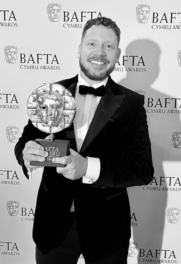 Ein Mann in einem Smoking, der eine BAFTA-Trophäe hält und lächelt, mit einem 'BAFTA Awards 2018'-Hintergrund.