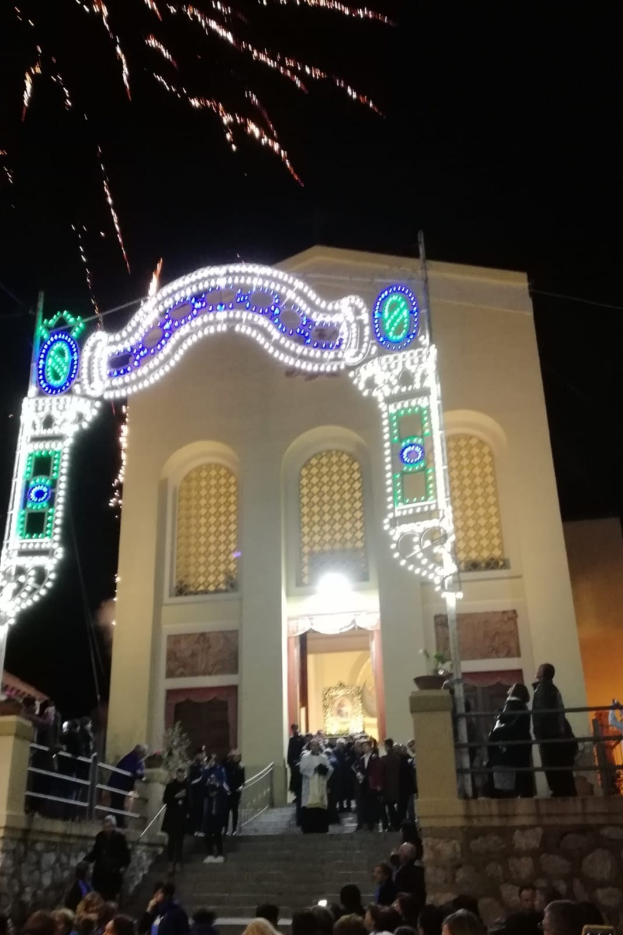 Menschen, die vor einem Gebäude mit einem beleuchteten Bogen, Treppen mit Geländern und Topfpflanzen stehen und Silvester mit Feuerwerken im Hintergrund feiern.