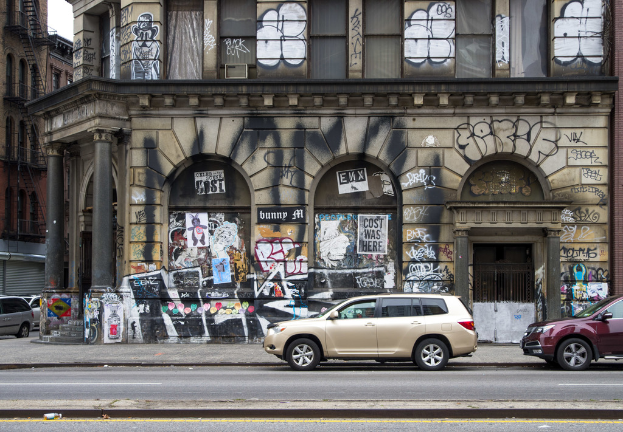 Gebäude mit Graffiti, Gittern, Treppen, Geländern, einem Himmel-Hintergrund und Kraftfahrzeugen auf der Straße.
