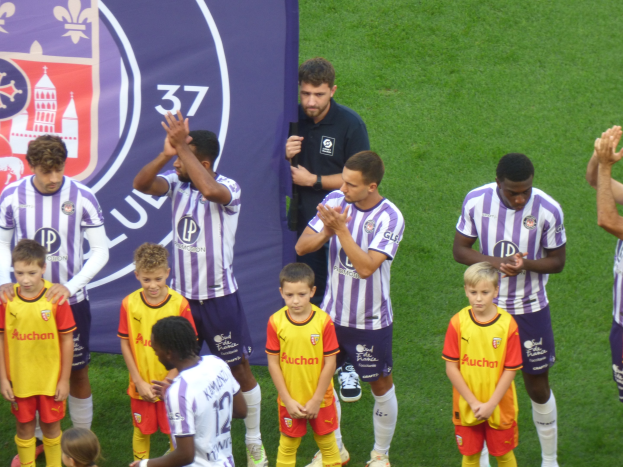 Gruppe junger Jäger auf einem Fussballfeld, die klatschen, mit einem Banner und Logos im Hintergrund.