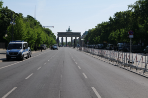 Ein Polizeifahrzeug parkt am Straßenrand vor dem Brandenburger Tor in Berlin, Deutschland, mit Barrieren, Hinweistafeln, Bäumen und Laternenmasten im Hintergrund und einer bewölkten Himmel.