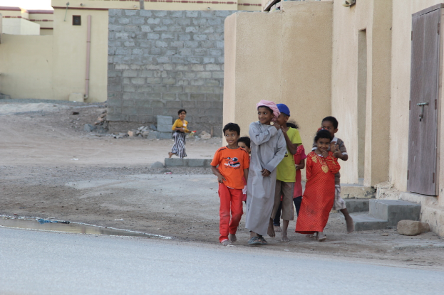 Eine Gruppe strahlender Kinder, die draußen vor Gebäuden, Wasser, Felsen und einer Straße steht.