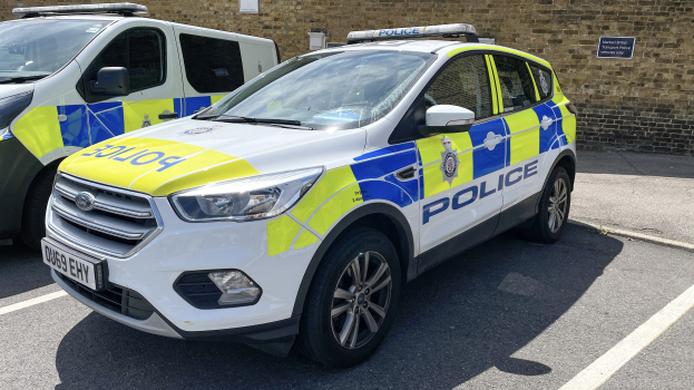 Zwei Polizeiautos nebeneinander auf einem Parkplatz geparkt, mit einer Wand und einer Tafel im Hintergrund.