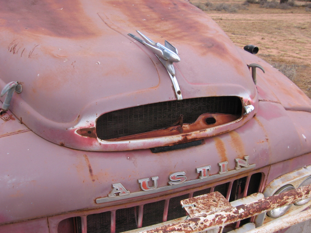 Alter rostiger Lkw auf einem Feld mit Bäumen und einem klaren blauen Himmel, der deutliche Rostspuren von langjähriger Witterungseinfluss zeigt.