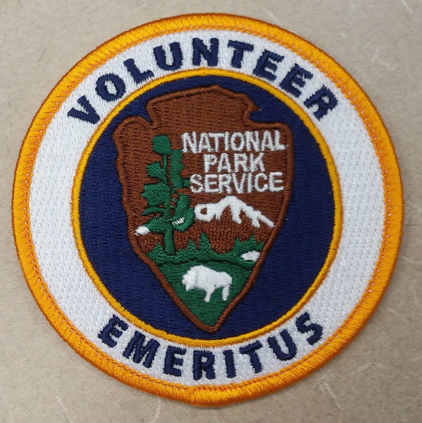 Runder Flicken mit blauem Rand und weißem Hintergrund, der schwarzen Text 'Volunteer National Park Service Emeritus' in der Mitte eines gelben Kreises zeigt.