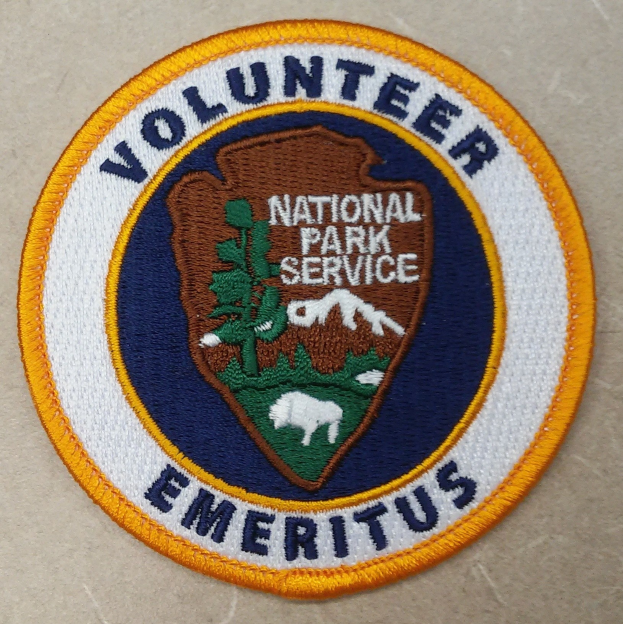 Runder Flicken mit blauem Rand und weißem Hintergrund, der schwarzen Text 'Volunteer National Park Service Emeritus' in der Mitte eines gelben Kreises zeigt.