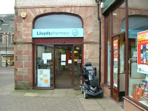 Eine Apothekenfiliale mit einem vor ihr geparkten Fahrzeug und einem Geb\344ude in der linken Ecke.