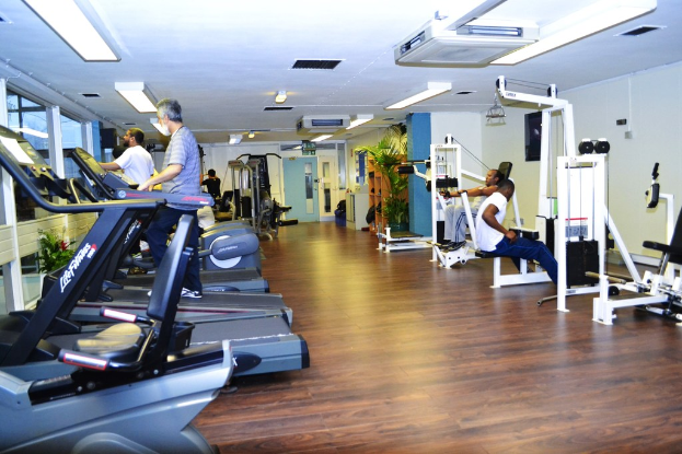 Ein Fitnessstudio mit verschiedenen Trainingsger├Ąten und Menschen, die trainieren, mit einer Pflanze auf der rechten Seite.