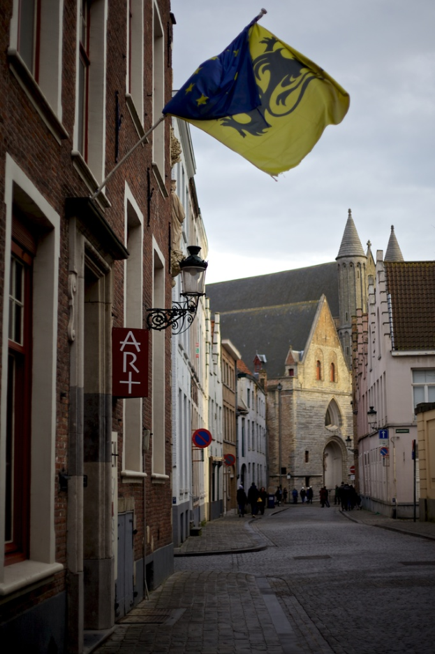 Eine Stadtansicht mit Gebäuden, Menschen auf der Straße, Pfählen, Schildern und einer Flagge an einem der Gebäude, unter einem Himmel.