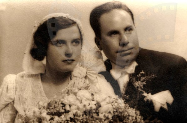 Ein Schwarz-Weiß-Foto eines strahlenden Mannes und einer Frau an ihrem Hochzeitstag, die Frau in einem weißen Kleid mit einem Bukett, der Mann neben ihr in festlicher Kleidung.