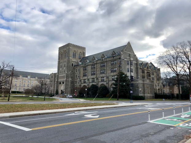 Großes Gebäude mit zahlreichen Fenstern, umgeben von Bäumen, Straßenlaternen, Ampeln und Fahrzeugen, unter einem bewölkten Himmel; als Campus der Universität Pennsylvania identifiziert.