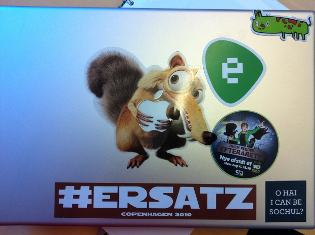 Ein Laptop und ein Buch auf einem Tisch, mit verschiedenen Stickern auf dem Laptop.