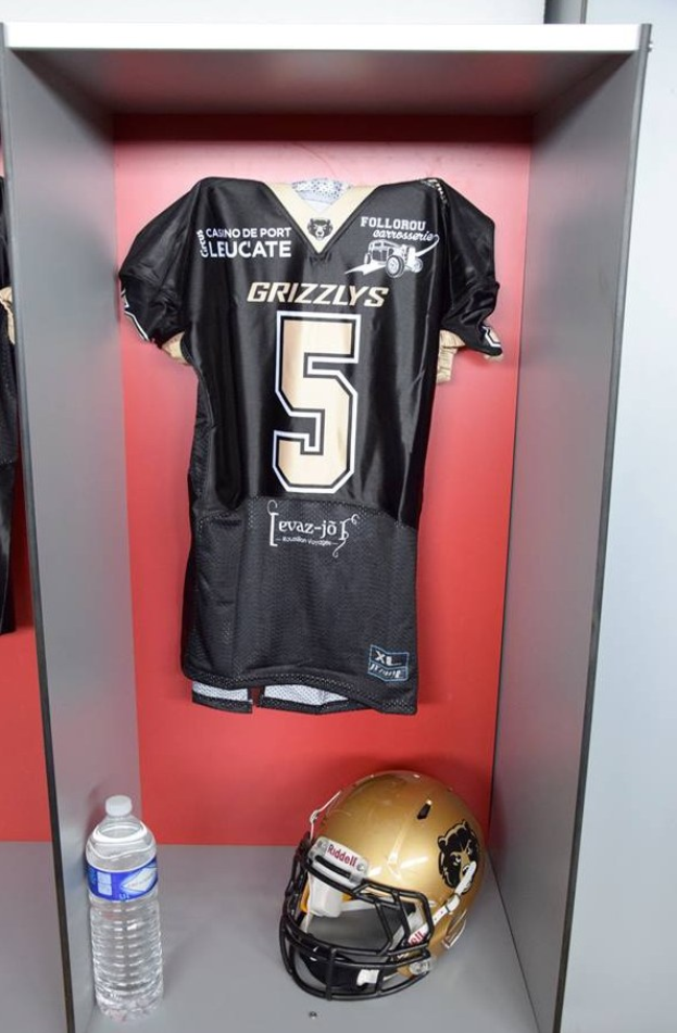 Ein Fussballtrikot und Helm h├Ąngen an einer Spindtür, mit einer Wasserflasche auf dem Regal darunter.