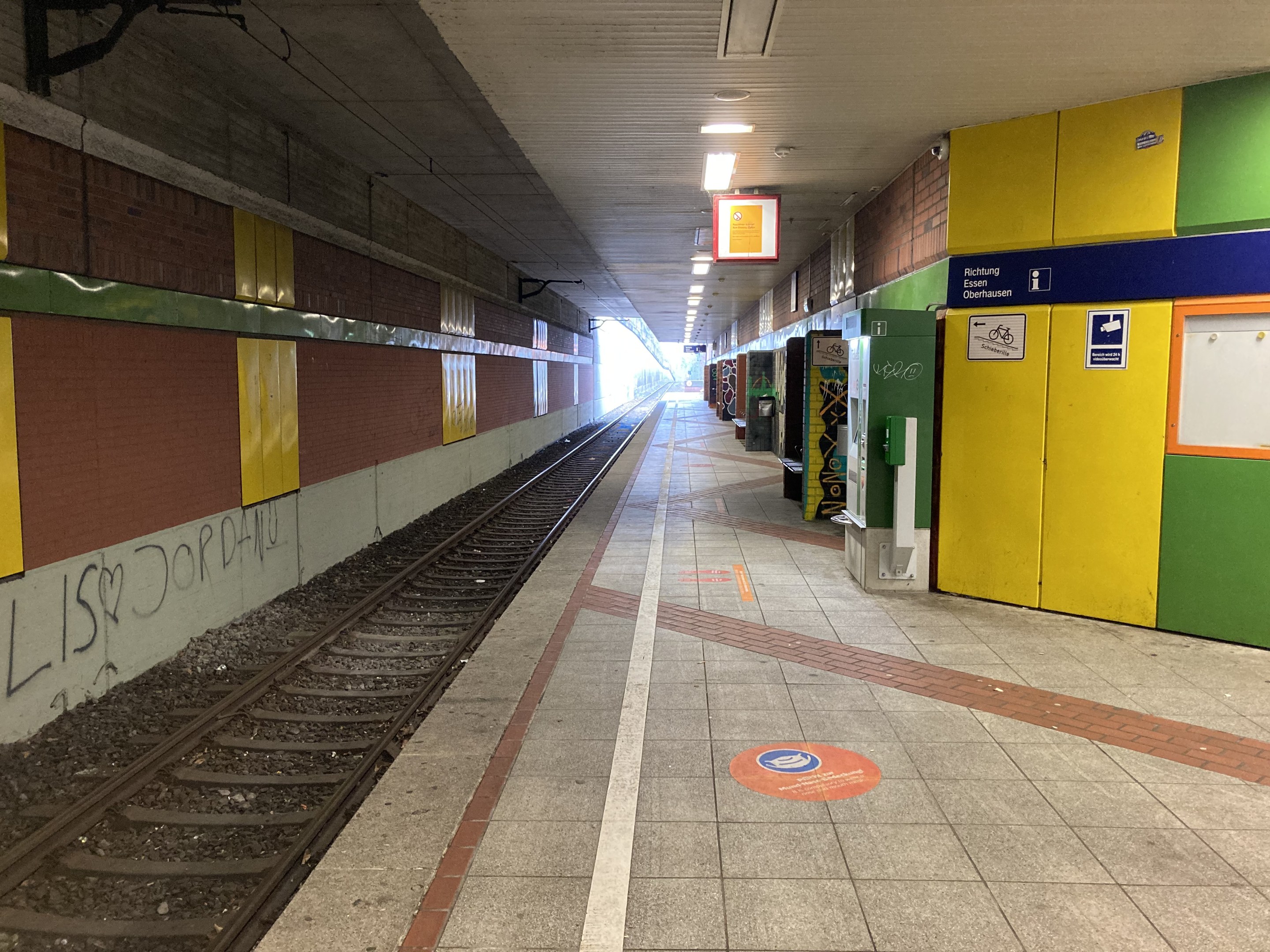 Ein Bahnsteig in Berlin Hauptbahnhof, Deutschland, mit einem Zug auf den Schienen, beleuchtet von Deckenlampen, einer Graffiti-bedeckten Wand auf der linken Seite und ein paar Gegenständen auf der rechten Seite.