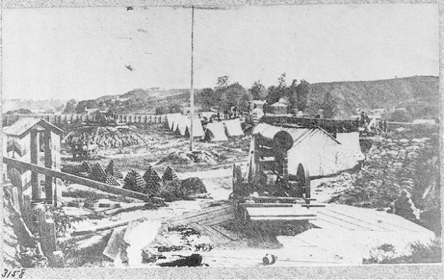 Schwarz-weiß-Foto einer Baustelle mit einer Maschine im Vordergrund, umgeben von Hütten, Bäumen, Hügeln und einem Himmel im Hintergrund, mit Text unten, der lautet: "Die Bauarbeiten an einer neuen Brücke in der Stadt San Francisco, Kalifornien."