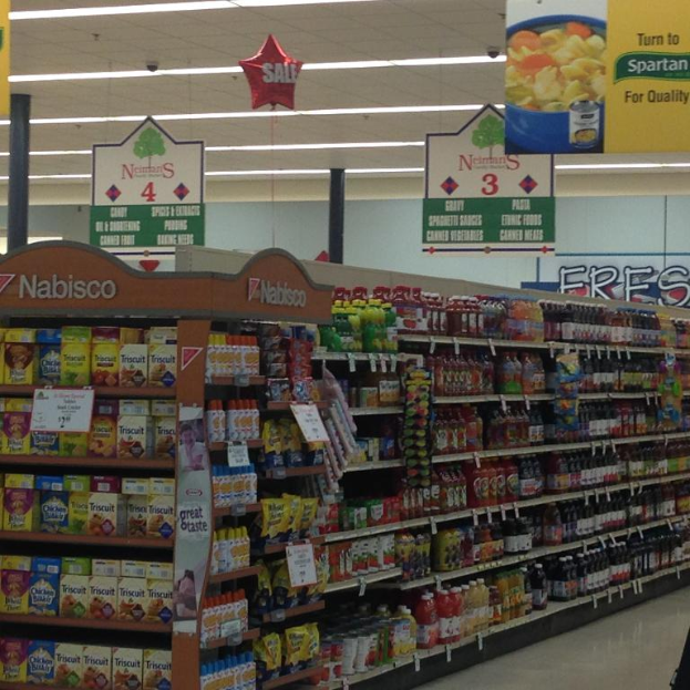 Ein Supermarktinneres mit Regalen voller Lebensmittel, Deckenlampen und Schildern.