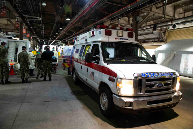 Ein Rettungswagen ist in einem Gebäude geparkt und von uniformierten Personen umgeben, mit verschiedenen Geräten und einer Jalousie im Hintergrund.