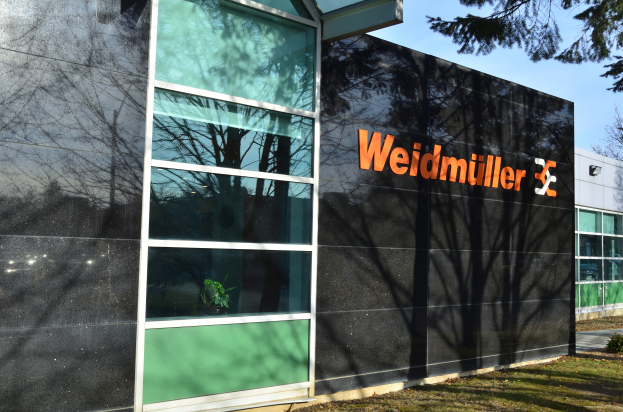 Die Weidmüller Group-Zentrale in Frankfurt, Deutschland, ein modernes Gebäude mit Glaswänden und Text auf der Fassade, umgeben von grünem Gras und Pflanzen, mit Bäumen und einem klaren blauen Himmel im Hintergrund.