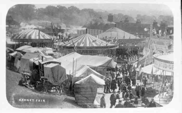 Ein altes Schwarz-Weiß-Foto einer belebten Karnevalszenen mit Zelten, Menschen, Wagen, Pfählen, Bäumen und Gebäuden im Hintergrund, beschriftet mit "Barnet Fair, London, England".