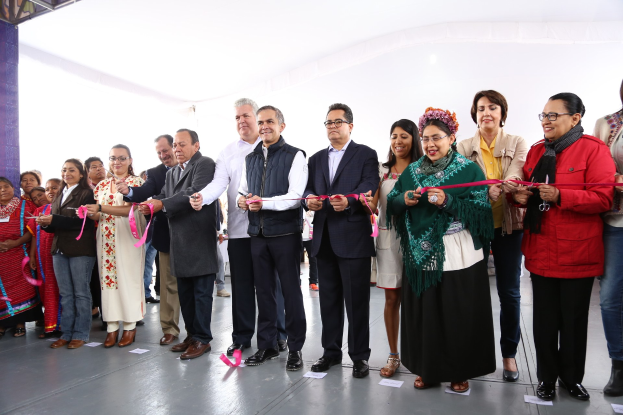 Eine Gruppe von Menschen, die strahlend eine Schere halten und Papiere auf dem Boden sowie ein weißes Tuch im Hintergrund.