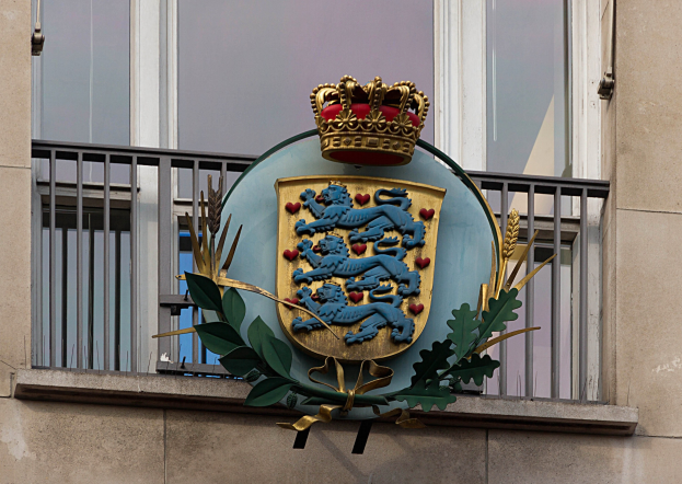 Wappen der britischen Königsfamilie auf einem Gebäude displayed, mit einer Krone und Blätter-Logo, Fenstern und Metallgittern im Hintergrund.