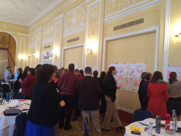 Eine Gruppe von Menschen, die Plakate und Charts an einer Wand in einem scheinbar künstlerischen Museum betrachten.