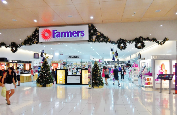 Menschen gehen durch einen Weihnachtsdekorationen Einkaufszentrum mit beleuchteten Bäumen, Dekorationen und einer Deckenbefestigungstafel, einige tragen Einkaufstaschen.