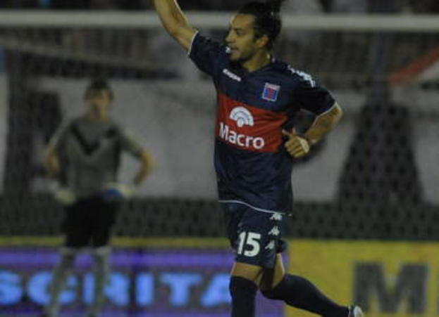 Ein Fußballspieler feiert nach einem Tor auf dem Boden, mit einer jubelnden Menge und einer Person im Hintergrund, alles vor einem unscharfen, energetischen Hintergrund.