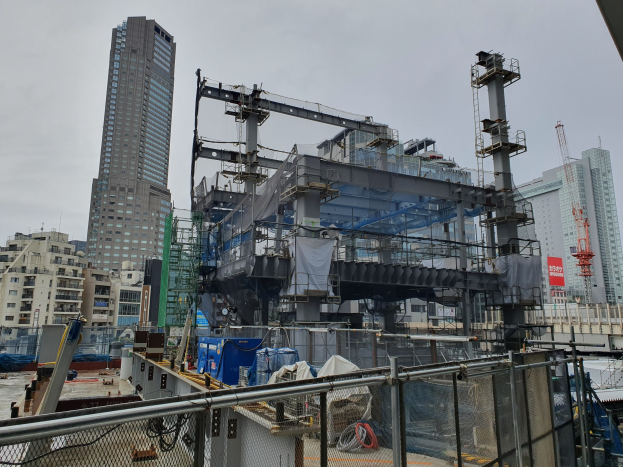 Großbaustelle für ein neues Kraftwerk in einer städtischen Umgebung, umgeben von einem Metallzaun, mit Gebäuden, Polen, einem Banner, Fahrzeugen, Drähten und einem bewölkten Himmel.