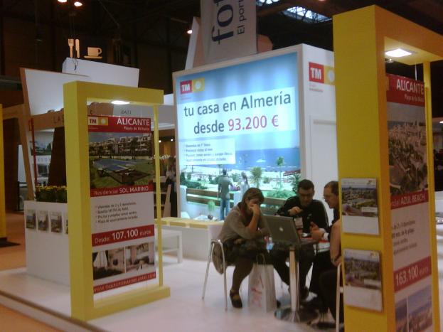 Eine Gruppe von Menschen sitzt um einen Tisch und schaut auf einen Laptop, mit mehreren Flyern mit verschiedenen Werbeanzeigen daneben.