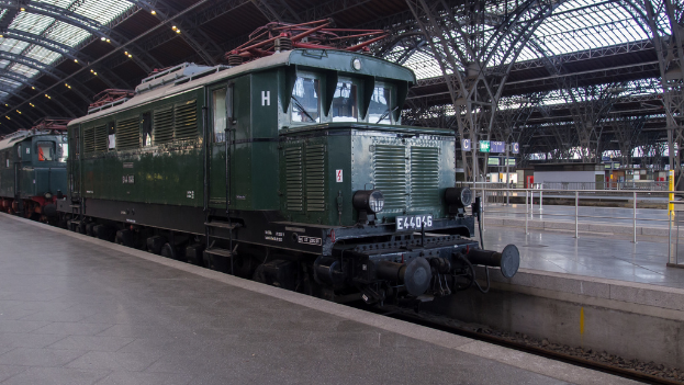 Ein Zug auf Schienen mit Geländern und Planken im Hintergrund, Lichter auf dem Dach und ein Himmel darüber, mit einem Boden darunter.