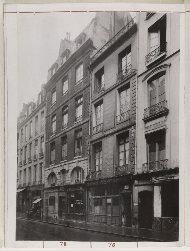 Schwarz-weißes Foto einer Stadtstraße mit Gebäuden, Fenstern, Geländern, Namensschildern und einer Straße unten.