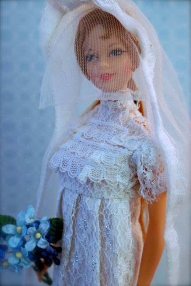 Eine Puppe in einem Kleid, Schleier und mit einem Strauß, vor einem unscharfen Objekt.