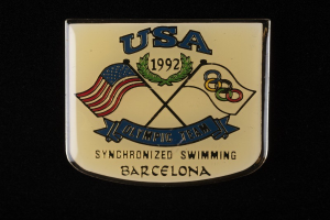 Abzeichen mit dem Text "USA Olympic Team Synchronized Swimming Barcelona" und zwei Flaggen (rot und blau) auf schwarzem Hintergrund.