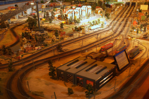 Eine detaillierte Miniatur-Modellbahnanlage in einem Museum, die Gebäude, Bäume, Schienen, Fahrzeuge, Pfosten, Lichter und Platten zeigt, die eine belebte Stadtlandschaft nachahmen.