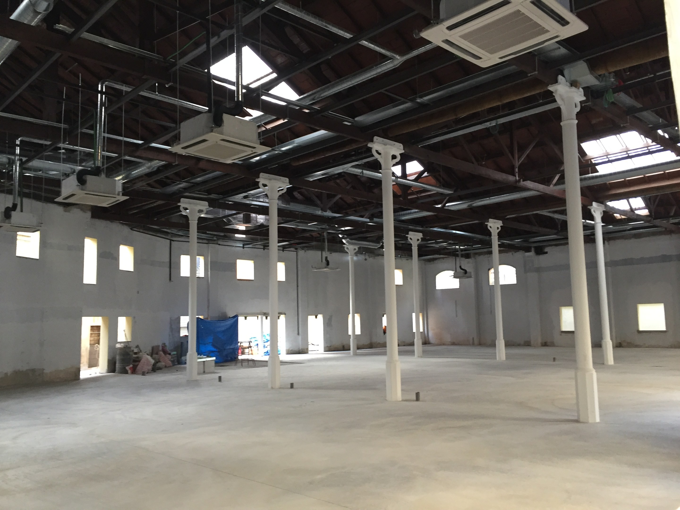 Industrielle Lagerhalle mit großen Fenstern, Säulen, Deckenleuchten und Klimageräten zur Miete verfügbar.