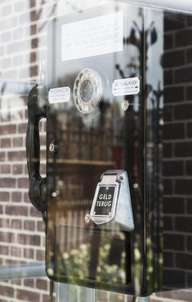Ein altmodisches Münztelefon steht auf einer Glasfenster.