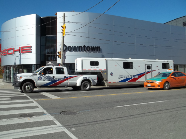 Ein vor einem Gebäude mit Text geparkter Polizeiwagen, ein Verkehrssignal mit Stange und Drähten im Vordergrund und Bäume mit einem klaren blauen Himmel im Hintergrund.