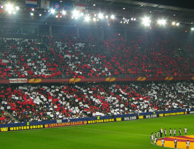 Ein Fußballspiel wird in einem großen, hell erleuchteten Stadion mit Zuschauern auf dem Feld und auf den Tribünen gespielt.