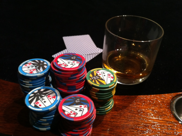 Eine hölzerne Oberfläche hält Münzen, ein schwarzes Tuch mit Karten und ein Glas mit Flüssigkeit.