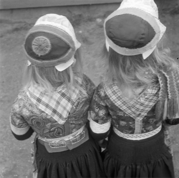 Zwei junge Mädchen in traditionellen bayrischen Trachten und Hüten stehen nebeneinander vor einer Wand, dargestellt in Schwarz-Weiß.