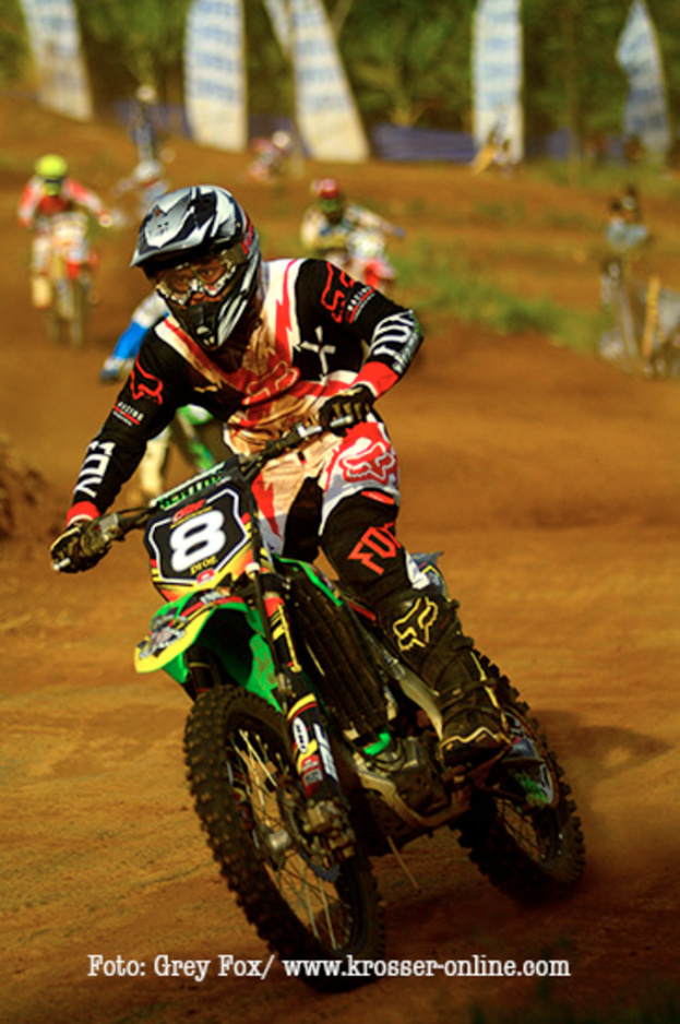 Mehrere Motorradfahrer mit Helmen rasen, mit Text unten im Bild.